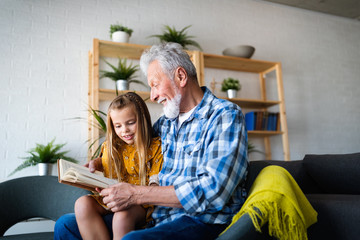 Happy little girl with grandfather reading story book at home