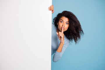 Photo of casual curly wavy beautiful brown haired girl showing you shh sign with forefinger touching her lips looking out of white banner isolated blue pastel color background - obrazy, fototapety, plakaty