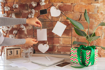 Wishes, dreams of goals plans on mood board aginst brick wall. Female hands on a background with wooden calendar, giftbox for New Year, winter holidays and Christmas time. Preparing moodboard.