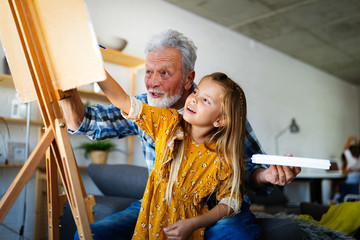 Senior man with child painting on canvas. Grandfather spending happy time with granddaughter.