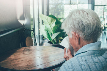 Old person coughing covering mouth with a tissue on a house interior. She has flu, allergy...