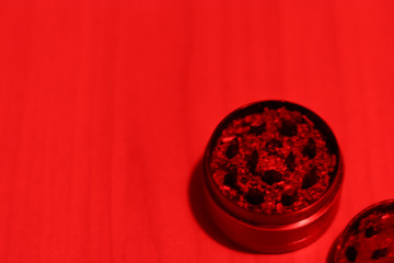 Ground medical marijuana close-up in a grinder. Preparing for smoking. Top view of accessories for drug use in red light