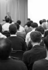 Obraz premium Speaker on the stage with rear view of audience in the conference hall or seminar meeting, business and education concept. Speaker giving a talk at business meeting. Seminar presentation photo.