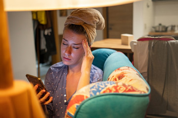 Woman upset after reading bad message on phone at home. Frustrated sad female crying, suffering, not in mood, thinking, depressed, stressed sitting on comfortable sofa holding smartphone.
