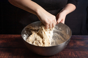 A cook in black kneads the dough in a metal bowl for cooking bread in the kitchen.