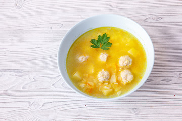 soup with meatballs in a white plate on a light wooden table