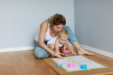 Mother with young baby doing early education lessons by using finger paints of pink and blue neon color on white paper - 304070339