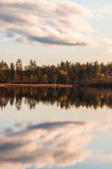 Sunset over a lake inside a forest in Sweden during autumn creating a perfect reflection of the trees and clouds in the water.
