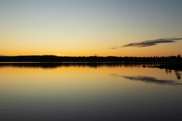 Naklejka na ściany i meble Sunset over a lake inside a forest creating a perfect reflection in the water. 