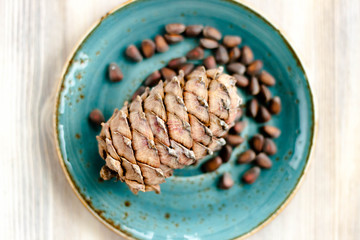 Pine cone and nuts on blue plate on wooden background. Healthy eating, organic food concept.