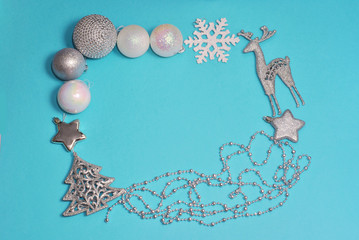 Christmas flat lay frame made from decorations silver and white color on the blue background. Toys decoration deer, stars, balls, beads, fir, spruce, fir-tree with free copy space for text. Winter