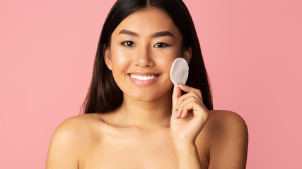 Beautiful asian girl cleaning face with cotton sponge