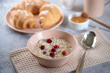 Oatmeal with milk and berries, and croissants with honey on the table. Tasty breakfast.