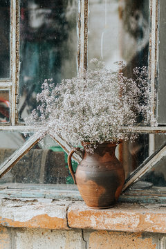 Beautiful retro still life with wild flowers in clay jug on windowsill of an old window.