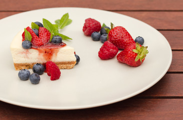 Close up of cheesecake with berries, coulis and mint on cream plate with wood background