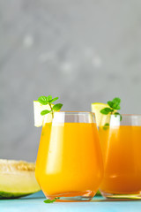 Yellow orange cocktail with melon and mint in glass on blue concrete background, close up