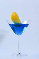 Cocktail with blue liquid in glass. Glass with blue water pouring with liquid with splashes and drops. Martini glass filling with alcohol with splashes on white background. Refreshing drink concept.