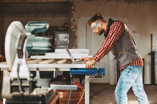 Young man work in home workshop using laptop and reads the manual