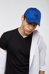 Cropped front view shot of a dark-haired man, wearing blue baseball cap with lettering 