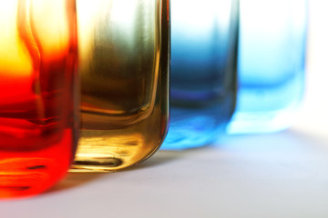 The lower part of colored transparent bottles for perfume or liquids on a light background. An example of color diffusion. Shallow depth of field. For articles about perfumes.