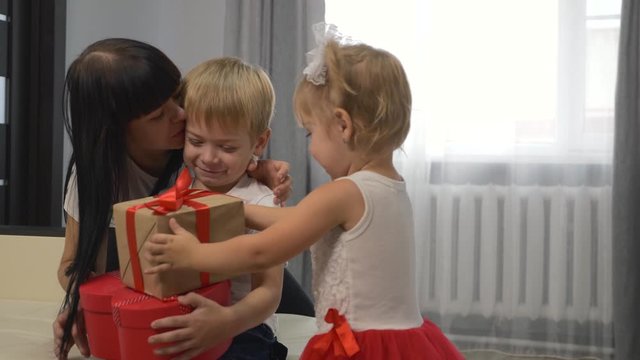 Happy young family at home. Loving mother and daughter give their beautiful son gifts for the holiday. Surprise for the son. The concept of family happiness. Teamwork.