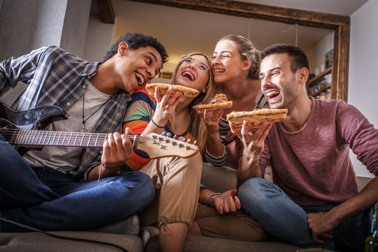 Group of friends making fun at the home party.They sitting in living room and eating pizza.
