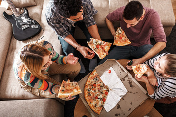 Group of friends making fun at the home party.They sitting in living room and eating pizza.