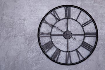 Vintage wall clock with roman numerals on the wall. gray stucco wall. Clock shows ten to twelve 11:50