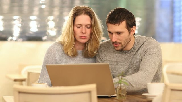 Front view of excited couple cheking laptop content sitting in a coffee shop in the 