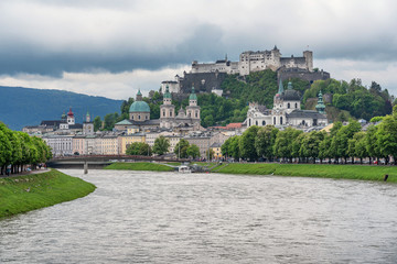 Fototapeta premium Classic panoramic view of historic city of Salzburg with famous Hohensalzburg Fortress and idyllic Salzach river on a beautiful day in spring with a dark dramatic cloudscape, Salzburger Land, Austria