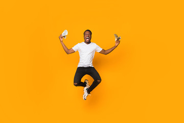 Fototapeta na wymiar Excited Afro Man Holding Money Jumping In Air, Orange Background