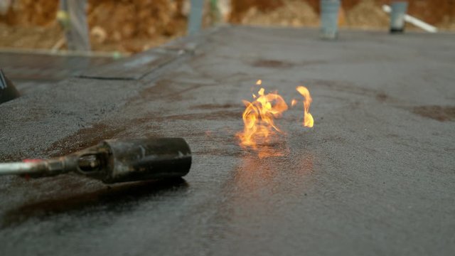 SLOW MOTION, CLOSE UP, DOF: Burning blowtorch melts tar covering the concrete foundation of a building under construction. Orange flames roll out of a torch after finished waterproofing process.