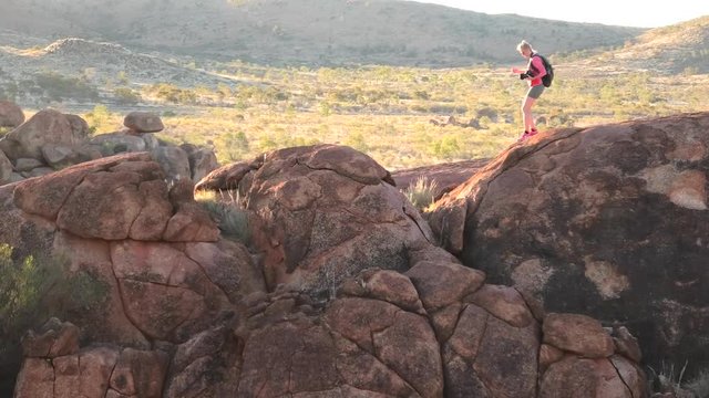Outback, Northern Territory, Australia. photographer woman rests after the trek to the top view of Karlu Karlu Devils Marbles. Traveler looking panorama over granite boulders at sunset light.