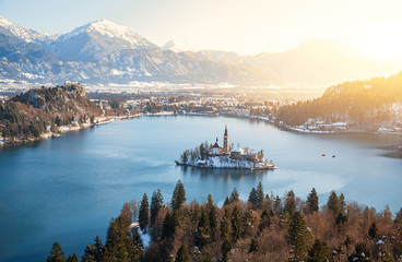 Panoramic aerial view of famous Bled Island (Blejski otok) at scenic Lake Bled with Bled Castle (Blejski grad) and Julian Alps in the background on a beautiful sunny day in winter, Slovenia