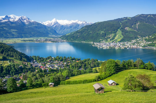 Panoramic view of beautiful scenery in the Alps with clear lake, green meadow, blooming flowers, traditional alpine chalets on a sunny day with blue sky in spring, Zell am See, Salzburger Land, Austri