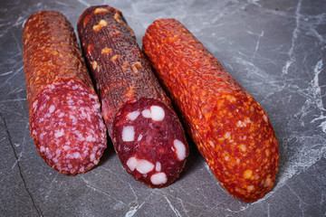 Three types of appetizing uncooked smoked sausages on a dark marble background.