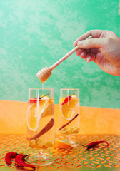 Drink in a glass with orange, cinnamon, chili pepper, honey and quince. Hand applying honey.	