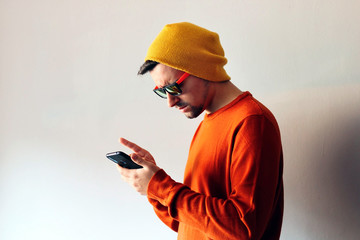 Young man dressed in orange with a yellow cpa and sunglasses looking an orientation app on his...
