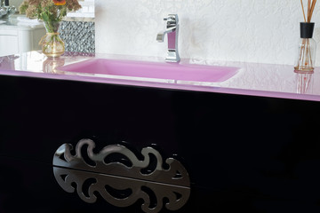 a sink made of glossy pink stone, in a fashionable interior, with a nightstand in black, with a designer handle, with flowers. washbasin in the bathroom