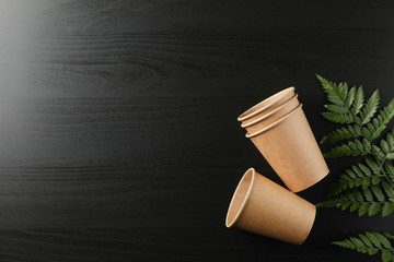 Eco - friendly cups and plant on black background, space for text