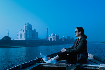 Fototapeta na wymiar Woman sitting on wooden boat in Yamuna River with Taj Mahal in background.