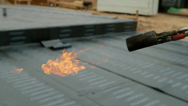 SLOW MOTION, CLOSE UP, DOF: Laborer's blowtorch is left lit up after hydroisolating a growing building. Detailed shot of flames as they come flickering out of the nozzle of a worker's propane torch.