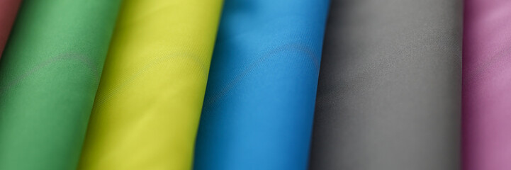 Close-up of many material tender silk on market of different colors green, yellow, blue, grey and burgundy. Fabric swatches stacked in pile. Fashion concept