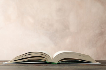 Opened book on wooden table against brown background, space for text