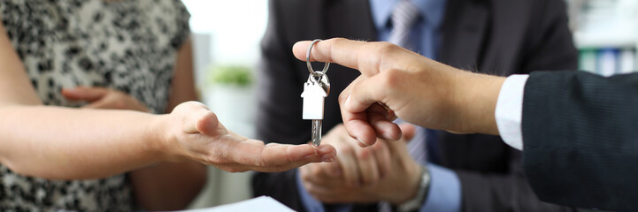 Focus on male hand giving house keys to new owner. Woman taking home keychain. Signing profitable...