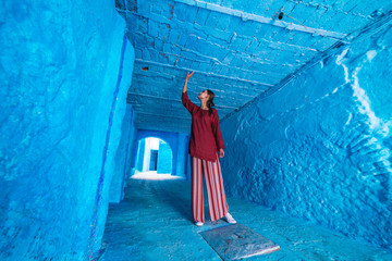 tourist in asian clothes stands in the tunnel of the blue city of morocco and touches the ceiling with his hand - 304091796