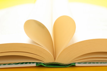Heart made of pages. Book on yellow background, close up