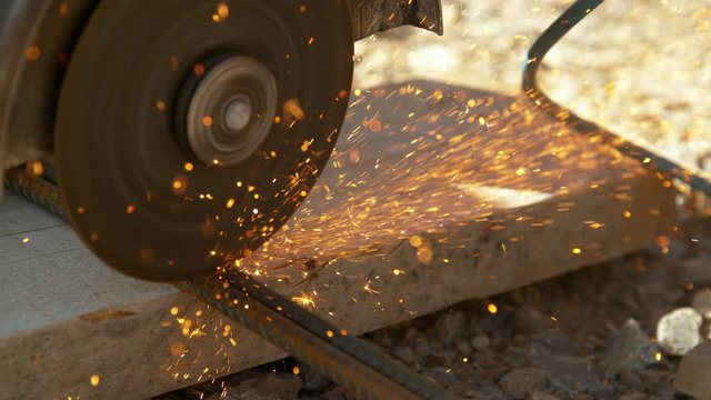 SLOW MOTION, CLOSE UP, DOF: Contractor cuts into two rusty metal rods with an angle grinder. Detailed view of laborer working at a construction site and cutting steel bars with a sharp circular saw.