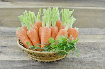 wicker basket with ripe carrots on wooden background