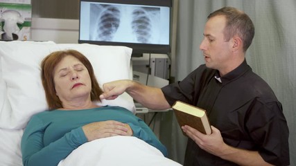 A priest delivers last rites to a woman who is near death in the hospital.